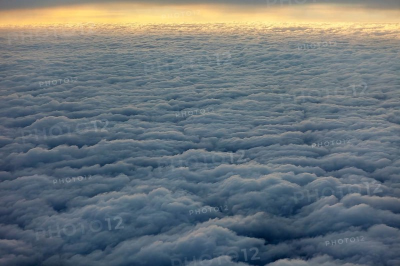 Dense, wavy cloud cover in grey sky, above the clouds on an airplane