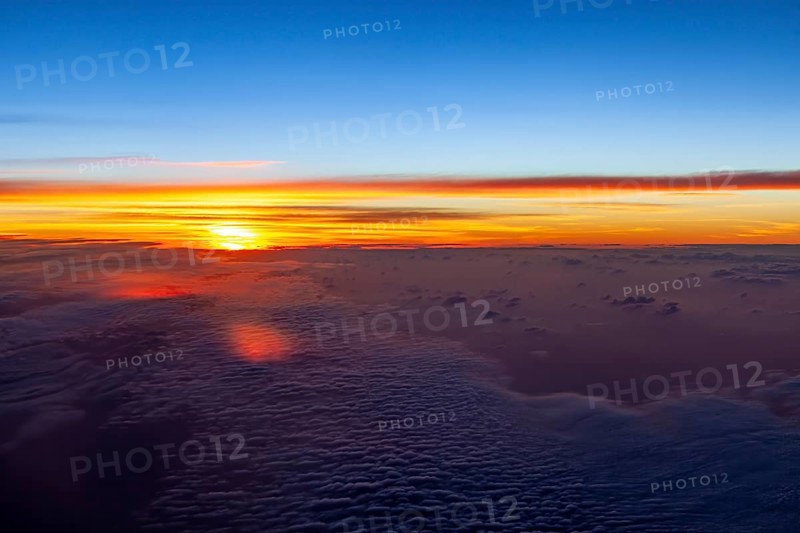 Bright colors of a sunrise over a cloud cover in the sky, on an airplane above the clouds