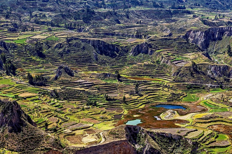 Landscape with terraced fields surrounded by mountains and a small lake under cloudy sky, The landscape of the Colca Canyon in the Andes of Peru
