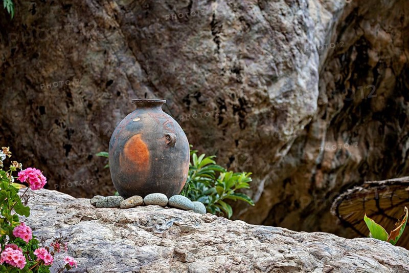 An ancient clay vase on stones in front of a rocky landscape with flowers in the foreground, a clay pot on a rock as decoration in the Colca Canyon in Peru