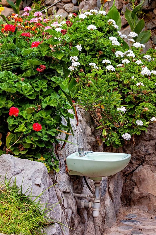 An outdoor garden with an old sink on a stone wall surrounded by colorful flowers, A sink in the garden in Colca Canyon in Peru