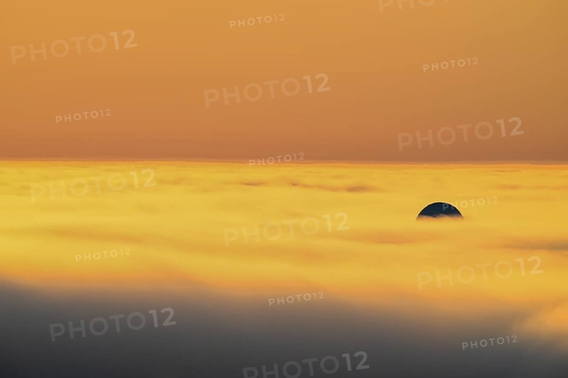 View from Mount Domen. Thick sea fog hangs over the Barents Sea and the midnight sun shines in an orange sky in the north. A dome of the NATO radar station in Vardö rises through the fog., Domen, Vardö, Finnmark, Norway