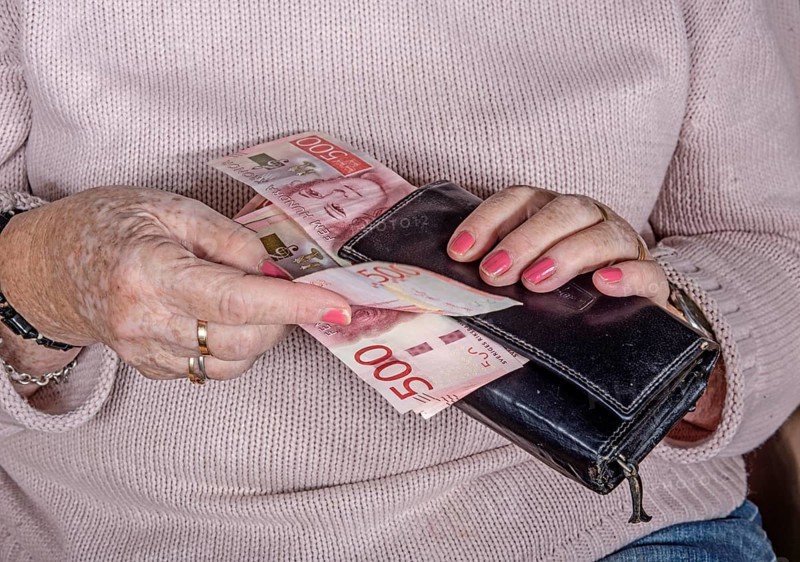 An elderly woman's hands take out Swedish banknotes from a wallet