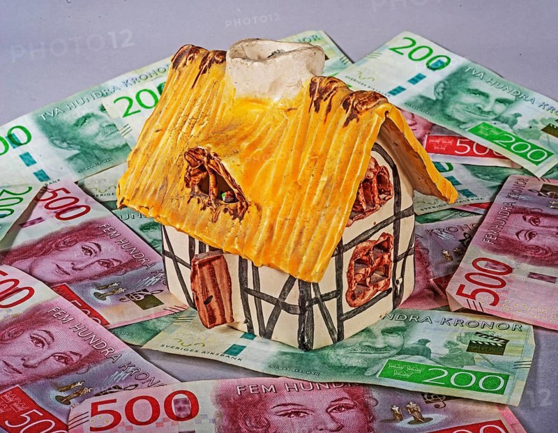 Small decorative ornamental cottage standing on Swedish 500 and 200 kronor banknotes. Symbol image