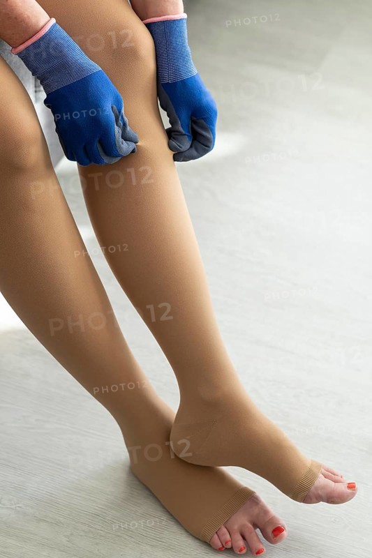 A woman sits at home and puts on medical compression stockings with special gloves on