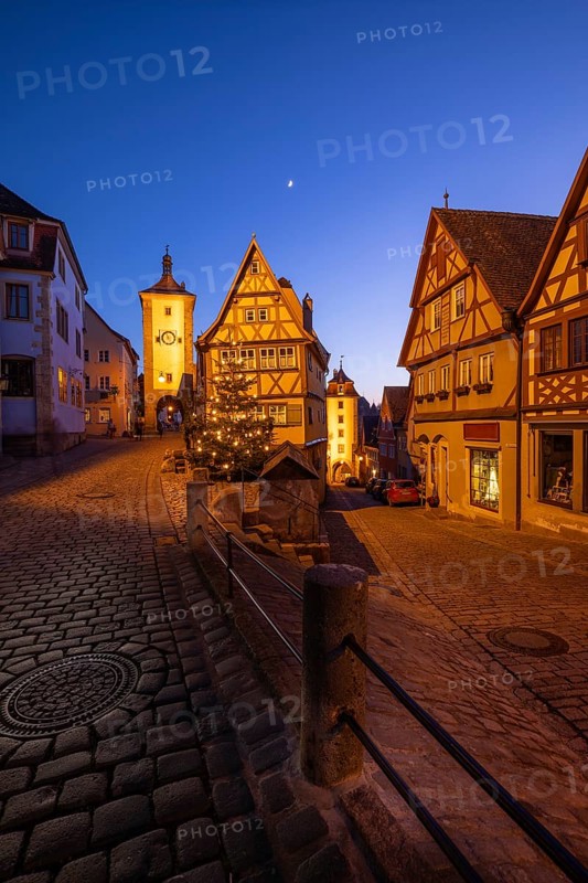 December 25, 2025: Christmastime at Plönlein — Rothenburg ob der Tauber, Bavaria, Germany. Festive Christmas tree and city lights at blue hour with moon in the sky