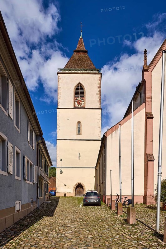 St. Martin parish church, church tower, church tower clock, houses, residential buildings, flagpoles, cobblestone street, parking strip with vehicles, blue sky, cumulus clouds, Kirchstraße, Staufen im Breisgau, Black Forest, Breisgau-Hochschwarzwald district, Baden-Württemberg, Germany