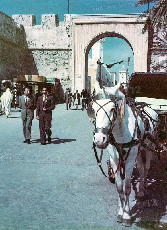 Horse drawn taxi in foreground, people walking in street, Bab al-Khendig archway city gate, Tripoli, Libya, North Africa 1956