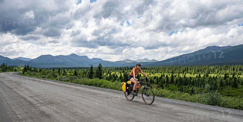 Young woman riding a bicycle on a dirt road through the tundra, mountainous landscape, Denali Park Road, Denali National Park and Preserve, Alaska, USA