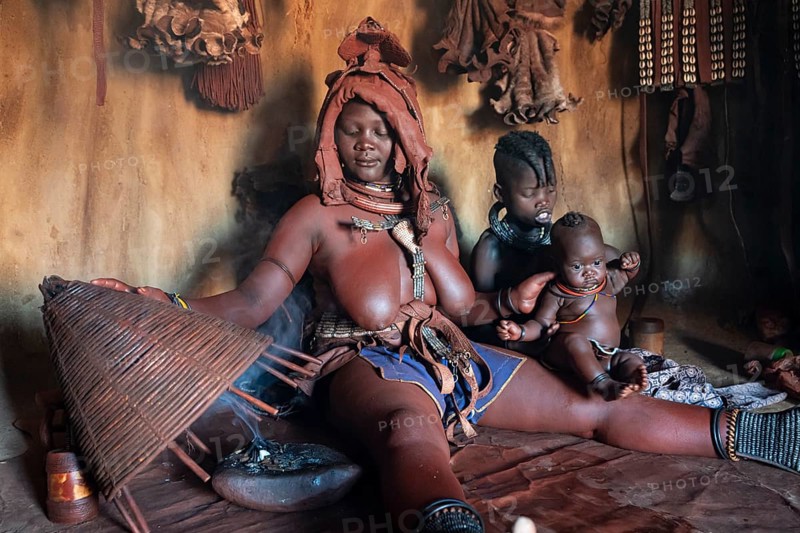Himba woman sitting with baby, Himba perfume, scented smoke from burning plants, Himba village, Kaokoveld, Kunene, Namibia