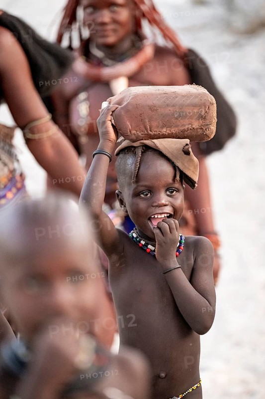 Himba woman and children run to fetch water with canisters through dry countryside, traditional Himba, Kaokoveld, Kunene, Namibia