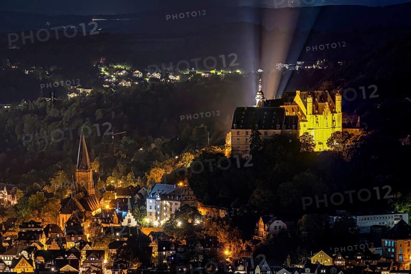 Castle and church shine in night lighting on a wooded hill. The Landgrave's Castle of Marburg in Hesse illuminated at night