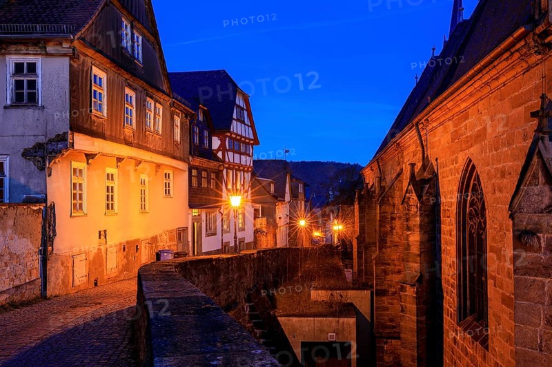 A nocturnal old town with half-timbered houses and cobblestones, warm lantern light creates a historic atmosphere, At the blue hour in Marburg city center in Hesse