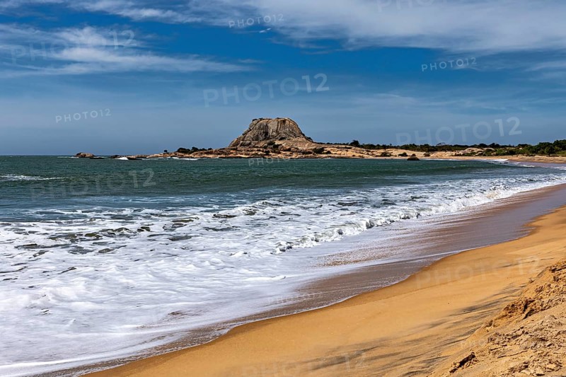 A peaceful coastal scene with sandy beach, turquoise ocean and distant rocks under blue skies, the scenery of Sri Lanka's Yala National Park