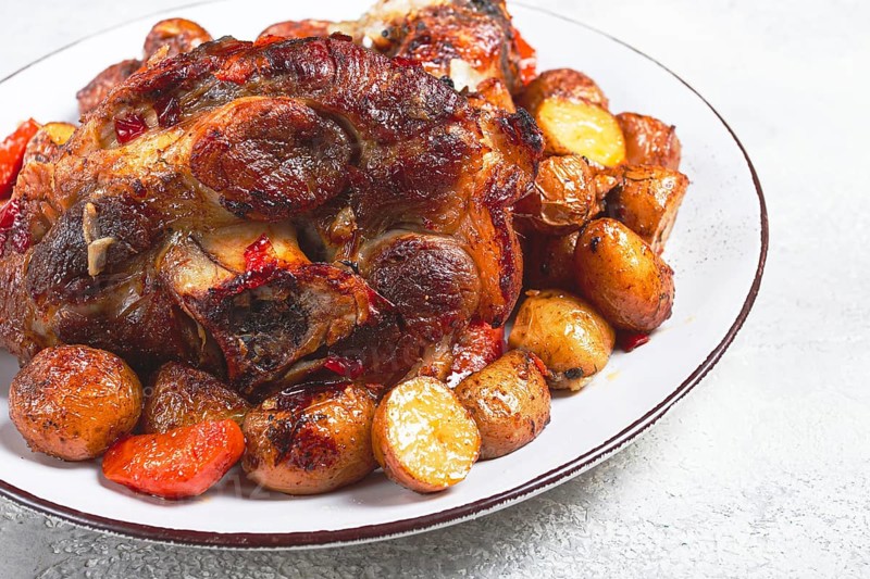 Pork knuckle baked with vegetables, new potatoes, on a white plate, homemade, no people
