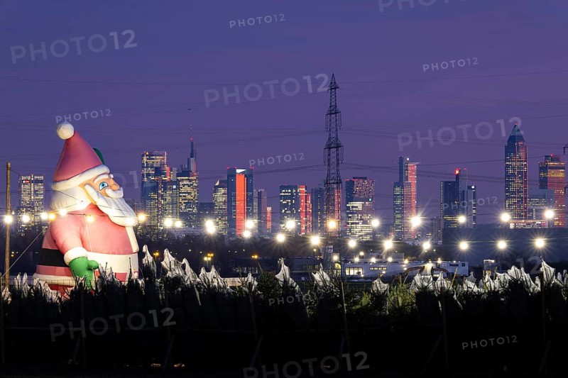 In a Christmas tree center near Frankfurt am Main, a multi-metre-high inflated figure of Santa Claus rises in front of the glowing banking skyline, Frankfurt am Main, Hesse, Germany