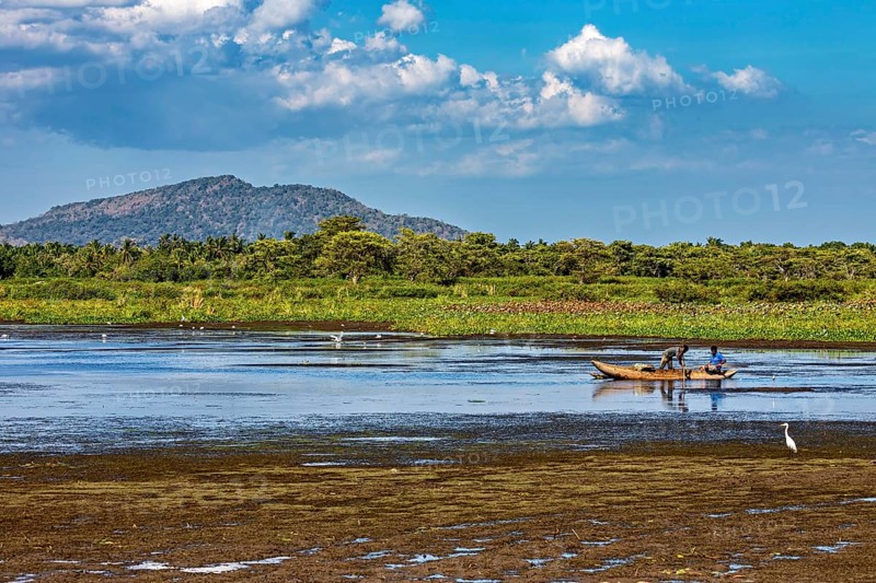 A small boat on a lake in a peaceful landscape with mountains in the background and a sky full of clouds, fishermen on a lake near Kandy in Sri Lanka
