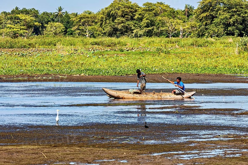 Two children paddle in a small boat on a quiet river surrounded by lush greenery and peaceful nature, fishermen on a lake near Kandy in Sri Lanka