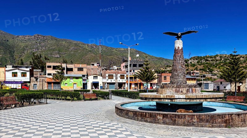 A public square with fountain and bird statue, surrounded by colorful houses and mountains, the town of Colca in Peru