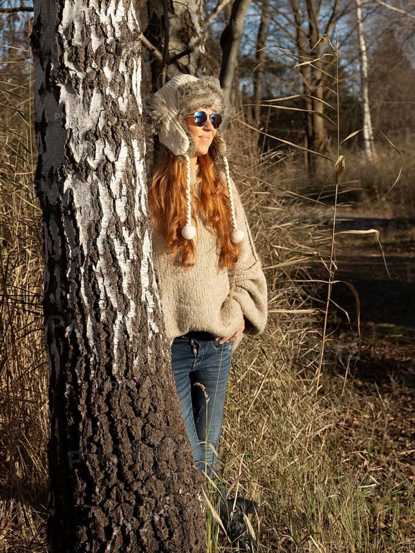 Slender pretty woman with fur hat and sweater, red hair and warm winter colors between birch forest and reeds