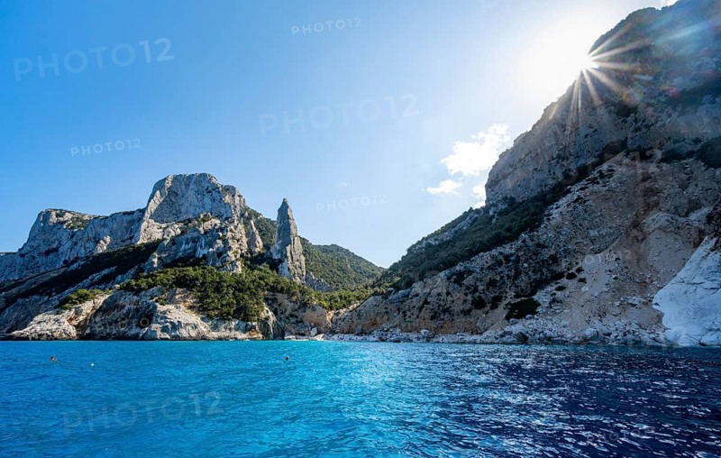 Picturesque rocky coast, cliffs with L'Aguglia pinnacle, blue sea and Cala Goloritzé beach, sun star, Golfo di Orosei, Baunei, Sardinia, Italy