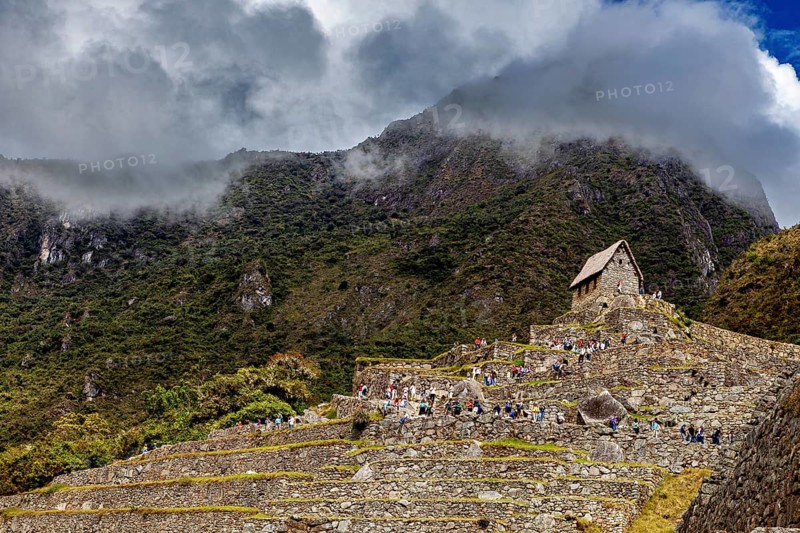Stone structures on steep terraces in front of a cloudy mountain, The ruins of the Inca city of Machu Picchu in Peru