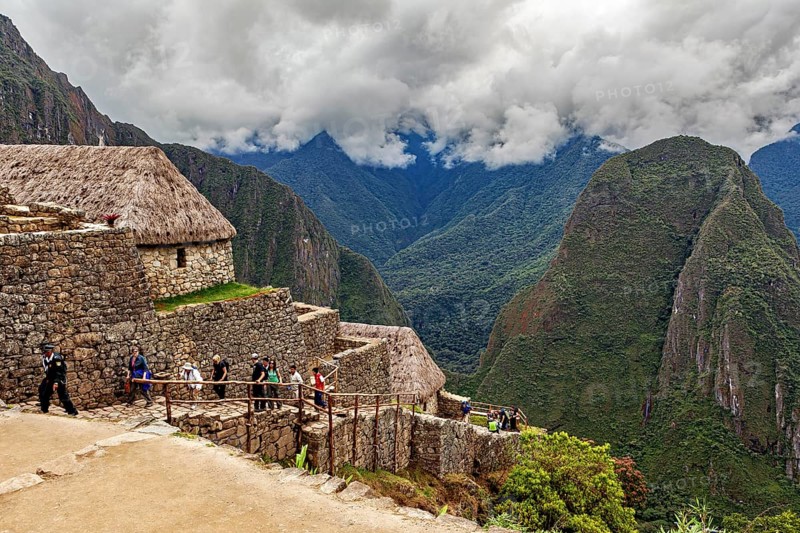 Hikers explore rocky ruins with thatched huts in a mountainous landscape, the ruins of the Inca city of Machu Picchu in Peru