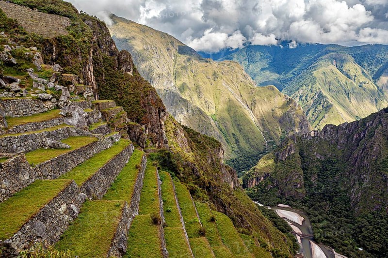 Green terraces over a river landscape under dramatic clouds, The ruins of the Inca city of Machu Picchu in Peru