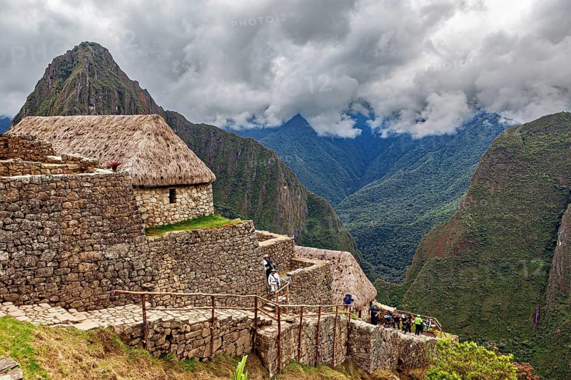 Historic ruins with grass-covered huts in the Andes against a cloudy sky, The ruins of the Inca city of Machu Picchu in Peru