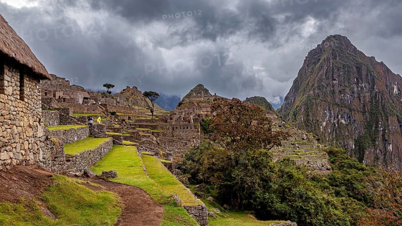 Ruins of Machu Picchu in the foreground against dramatic skies with thick clouds and green areas, The ruins of the Inca city of Machu Picchu in Peru