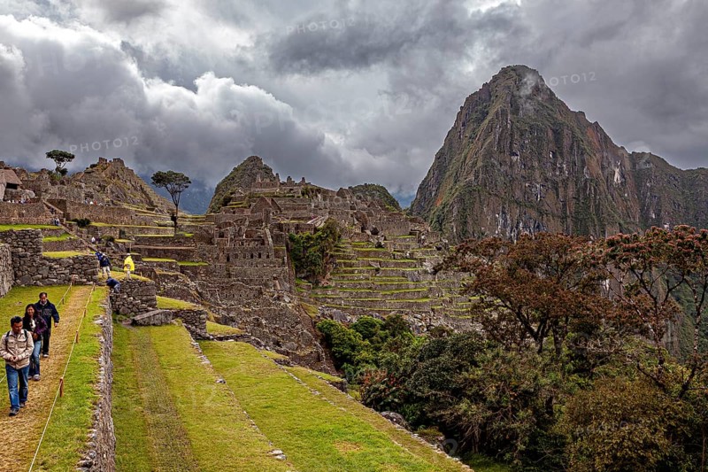 Walkers explore the ruins of Machu Picchu in front of dramatic mountain scenery, The ruins of the Inca city of Machu Picchu in Peru