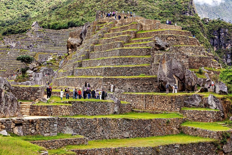 Ruins on terraces full of visitors with surrounding mountains and dramatic clouds, The ruins of the Inca city of Machu Picchu in Peru
