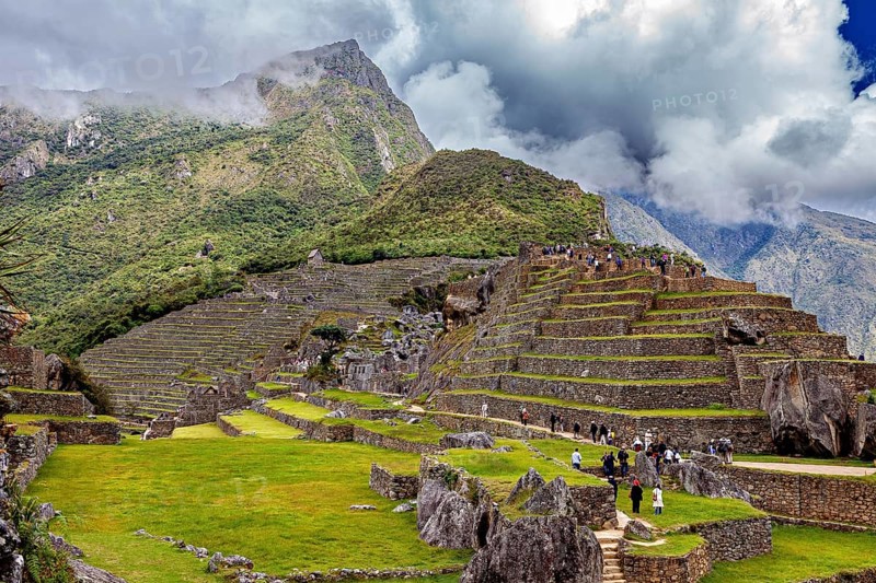 Stepped terraces with ruins against a dramatic mountain backdrop full of clouds, The ruins of the Inca city of Machu Picchu in Peru