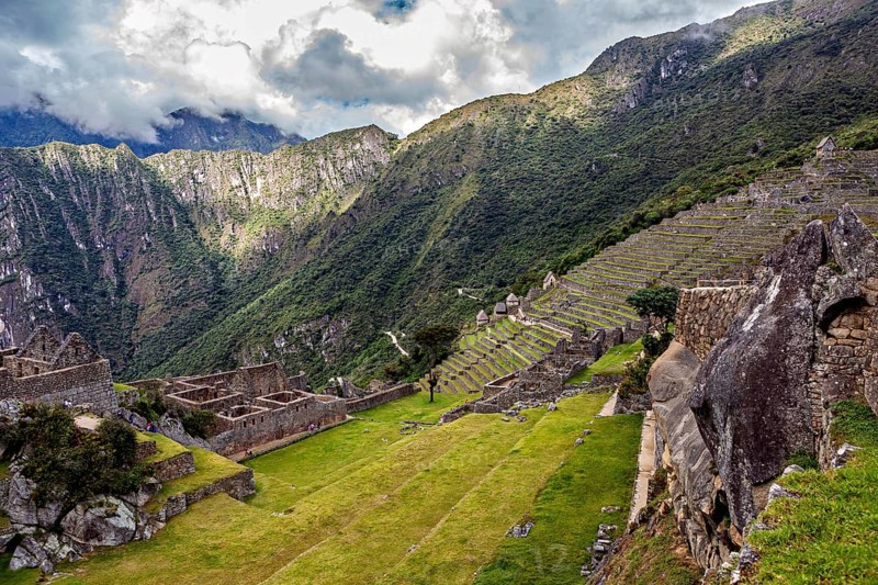 Descending terraces of ruins against mountain backdrop and cloudy sky, The ruins of the Inca city of Machu Picchu in Peru