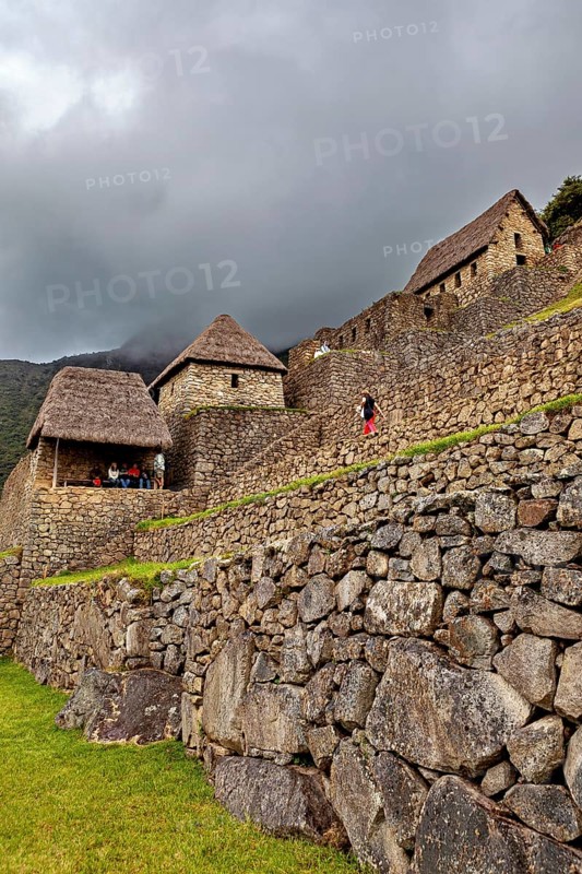 Stone walls and traditional houses against a dramatic, cloudy sky, the ruins of the Inca city of Machu Picchu in Peru