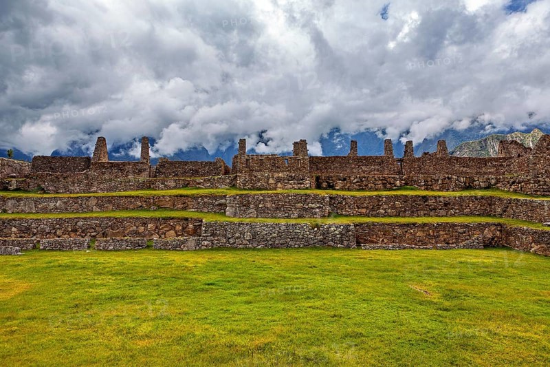 Plain with ancient stone ruins and grassy surfaces under a cloudy sky, The ruins of the Inca city of Machu Picchu in Peru