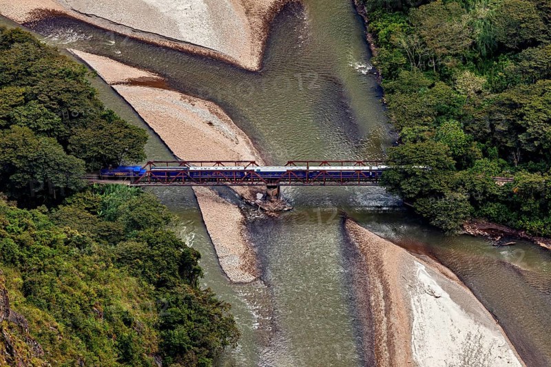 Train on a bridge over a river through a wooded landscape with sandbanks, view of the Urubamba Valley near Machu Picchu in Peru