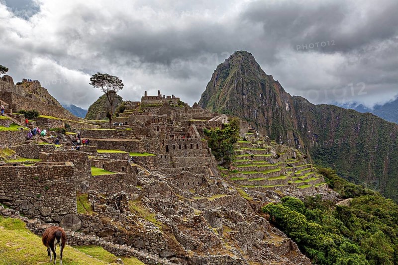 Historic ruins of Machu Picchu against a cloudy mountain backdrop with tourists, The ruins of the Inca city of Machu Picchu in Peru