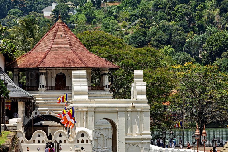 A temple with a pavilion surrounded by colorful flags and a river in the background, The Temple of the Tooth in Kandy Sri Lanka