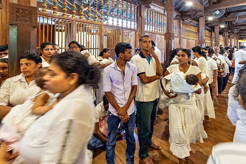 People stand in line in a traditional building, some carry babies, people and pilgrims in the Temple of the Tooth in Kandy Sri Lanka