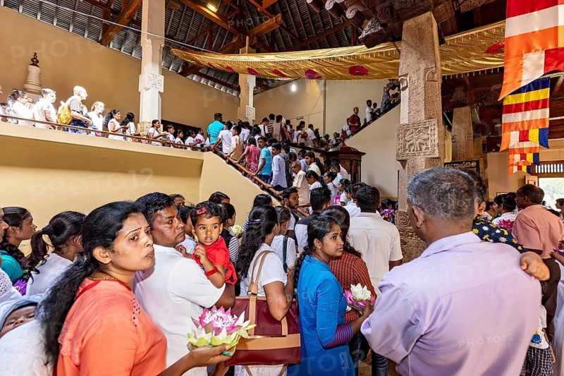 People gather in a decorated building for a religious ceremony with flowers, people and pilgrims at the Temple of the Tooth in Kandy Sri Lanka