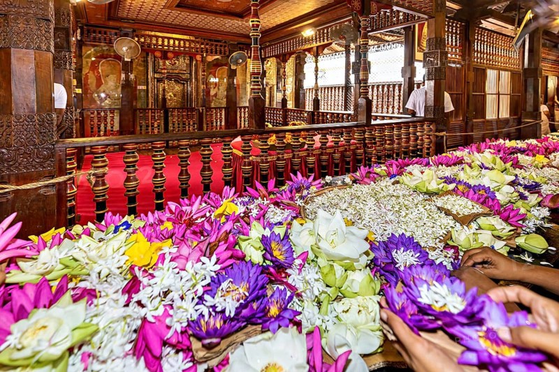 Colourful floral arrangements on an altar in a richly decorated wooden building, people and pilgrims in the Temple of the Tooth in Kandy Sri Lanka