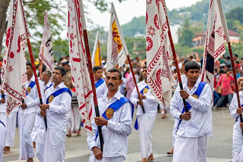 Participants wearing festive white uniforms carry red and white flags in a celebratory parade, The Perahera Parade in Kandy Sri Lanka