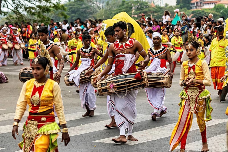 Participants in traditional outfits and drums at a cultural parade, spectators in the background, The Perahera Parade in Kandy Sri Lanka