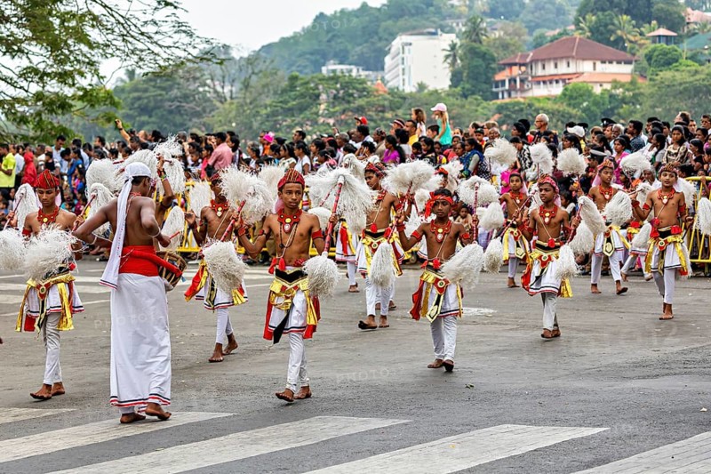 Children in festive dance costumes move happily through the streets, watched by spectators, The Perahera Parade in Kandy Sri Lanka