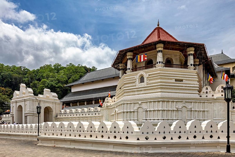 Temple complex with white wall, pavilion and colorful flags on a clear day, The Temple of the Tooth in Kandy Sri Lanka