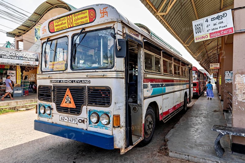 An Ashok Leyland bus at a busy bus stop in Sri Lanka, surrounded by signs and passers-by, bus station in Kandy Sri Lanka