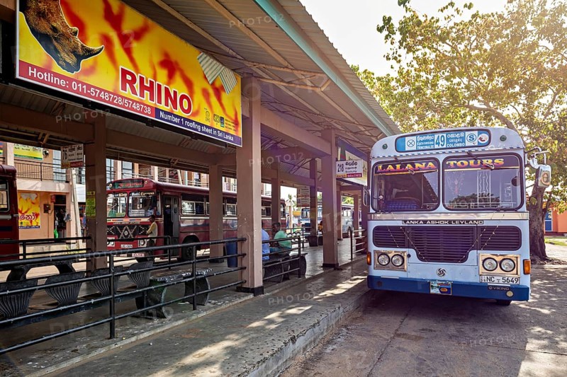 An Ashok Leyland bus at a bus stop with signs and trees in Sri Lanka, bus station in Kandy Sri Lanka