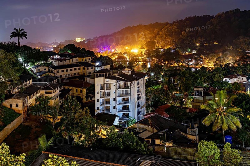 City at night with illuminated buildings and lush vegetation in hilly surroundings, conveys a lively atmosphere, view of the city of Kandy in Sri Lanka at night