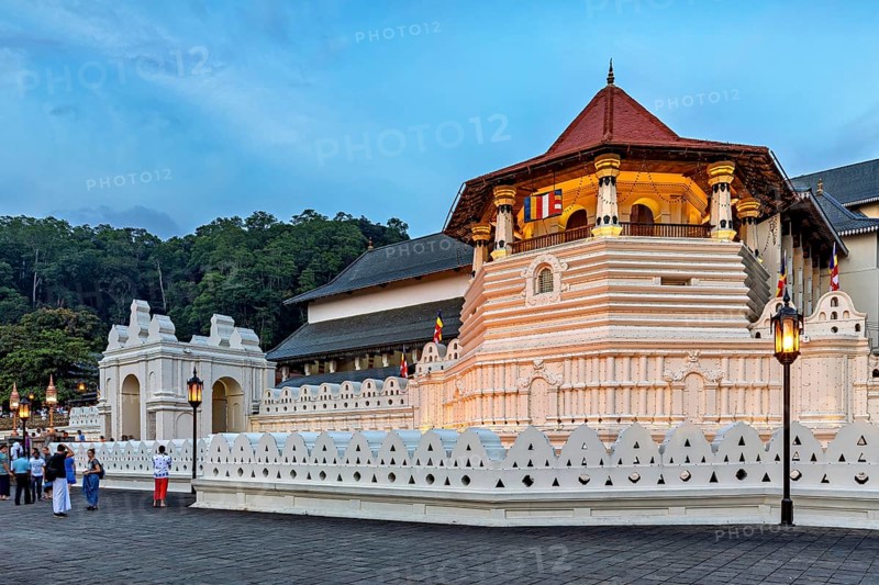 Historic building illuminated at dusk with visitors in the foreground, The Temple of the Tooth in Kandy Sri Lanka